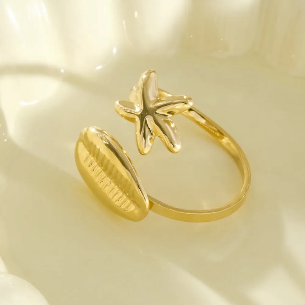 Anillo dorado abierto estrella de mar cauri puesto en el dedo