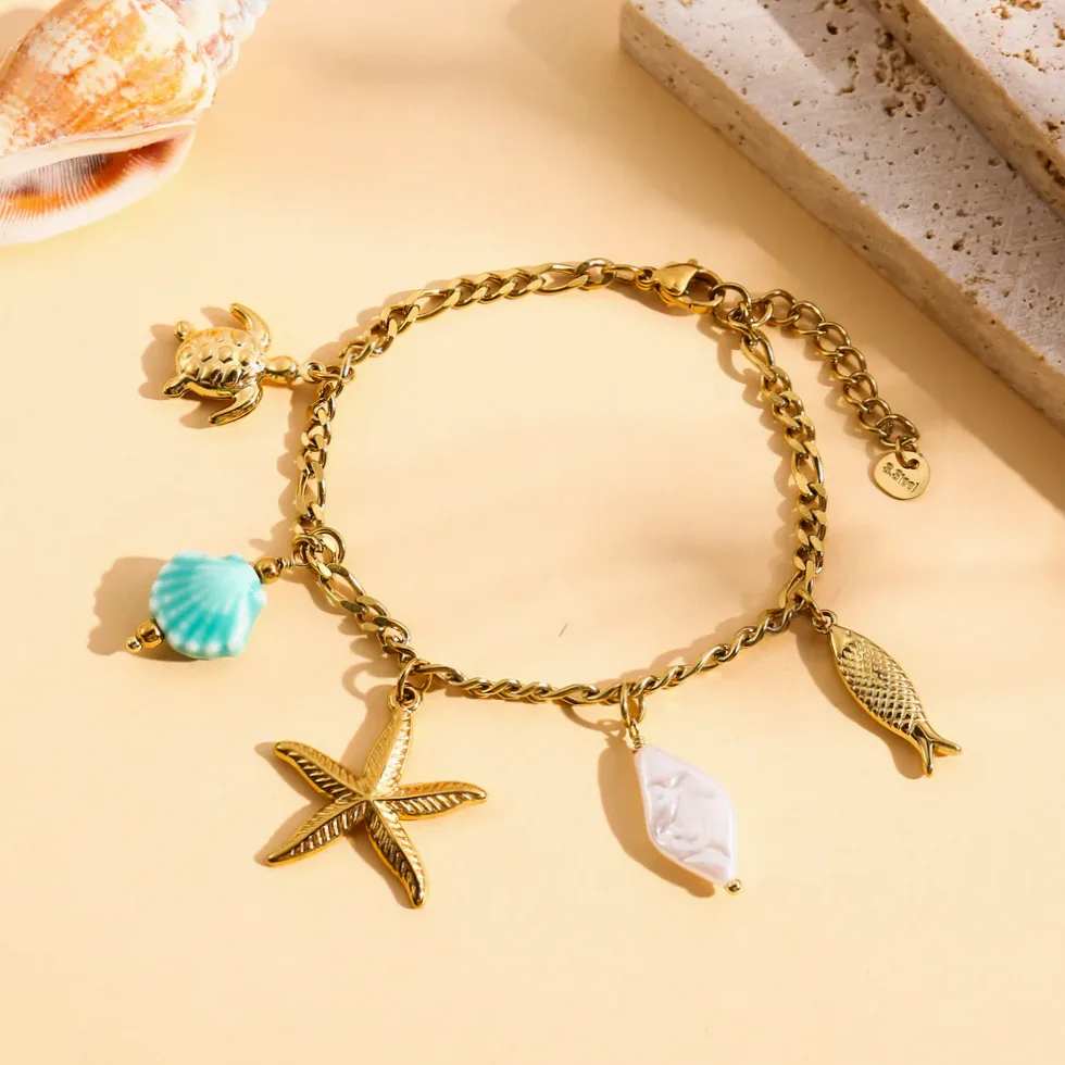 Detalhe do material e do acabamento — Pulseira dourada charms marinhos concha azul e pérola