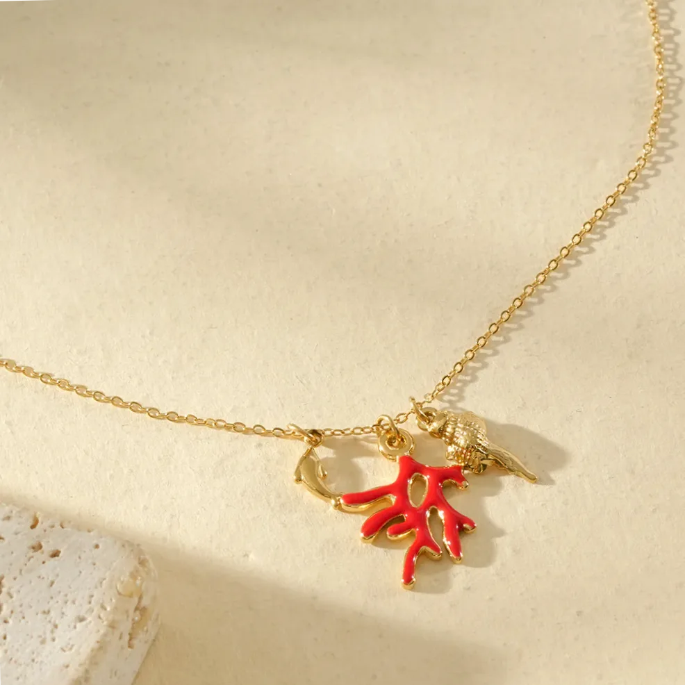 Dettaglio del materiale e della finitura — Collana dorata sottile pendenti corallo rosso e delfino
